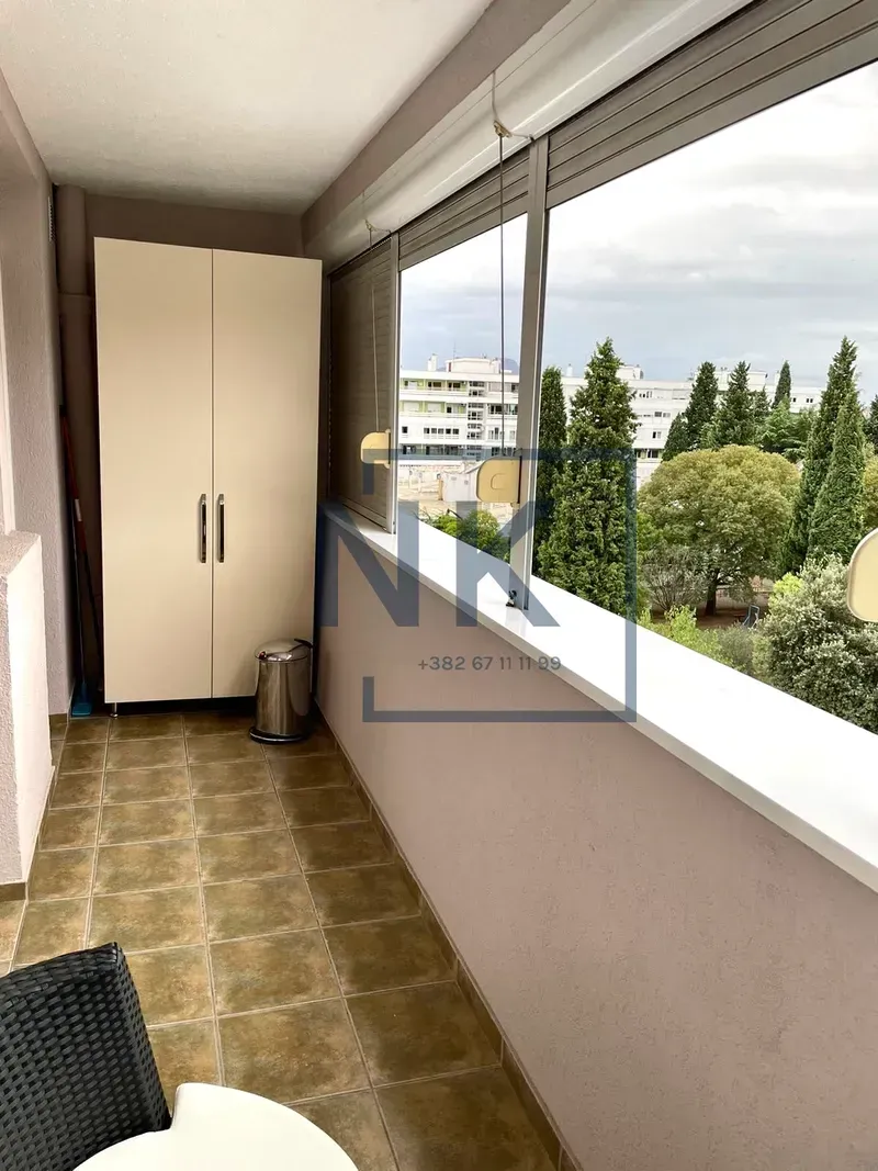 Enclosed balcony with a wardrobe and a view of surrounding buildings and greenery.