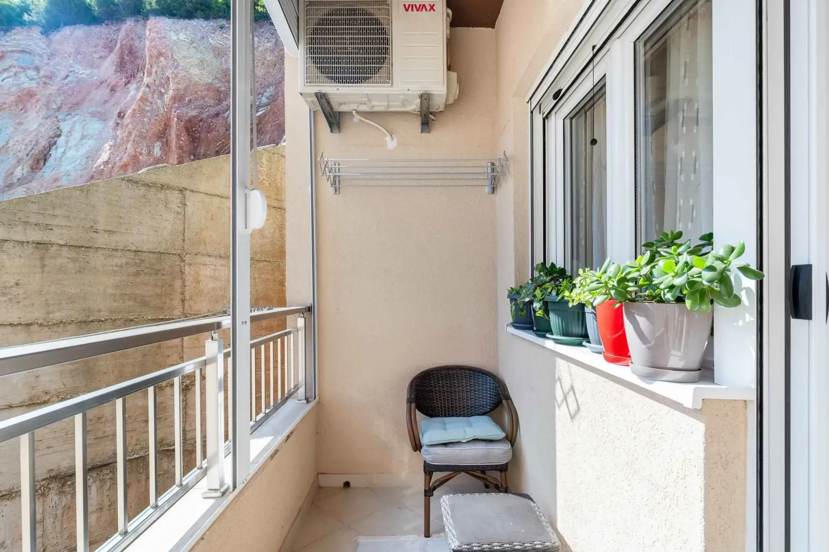 Manji zatvoreni balkon sa stolicom, klima uređajem i saksijama sa cvijećem.