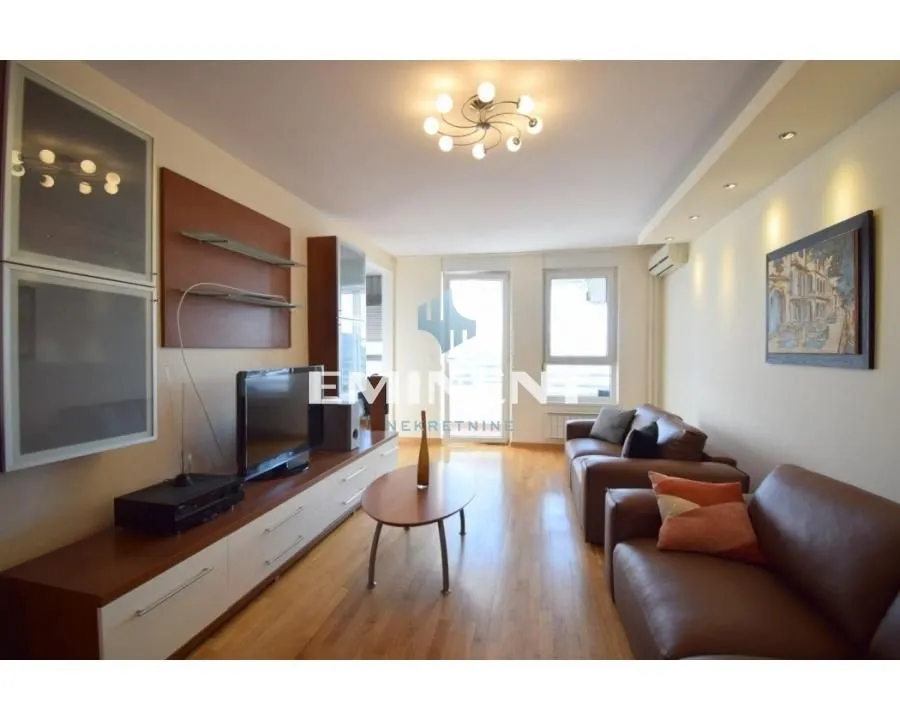 Spacious living room with seating set, television, and wooden flooring.