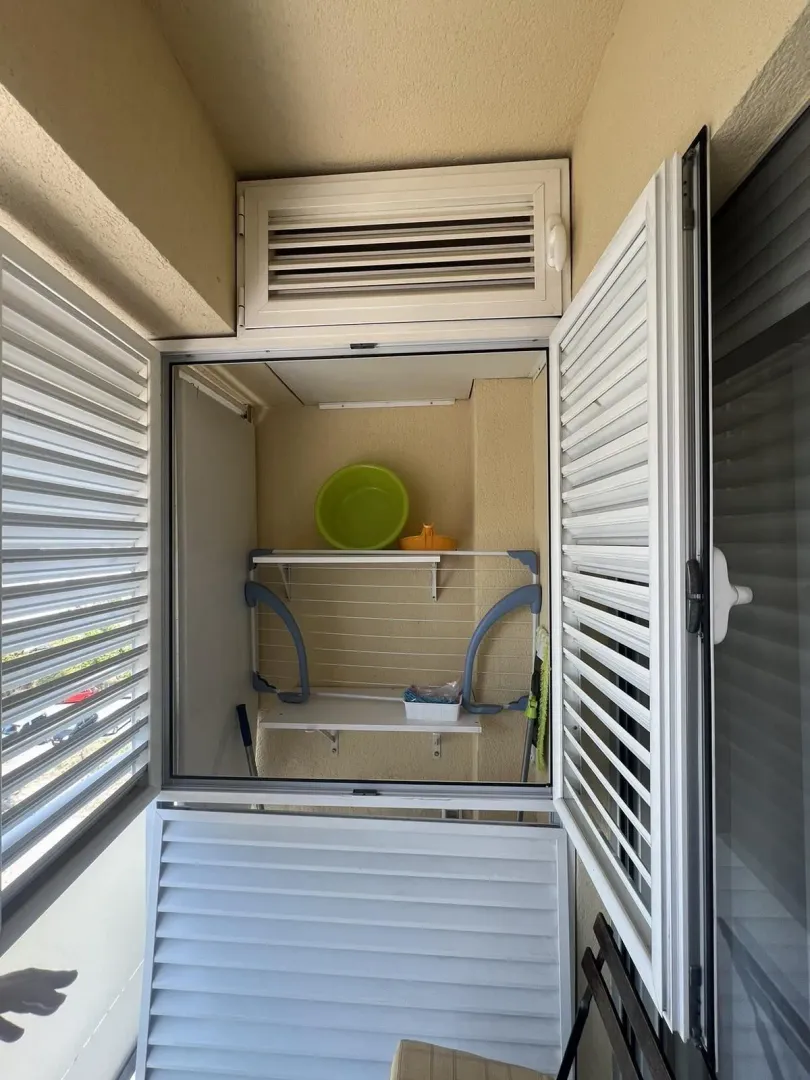 An enclosed storage niche on a balcony with white shutters and shelving.