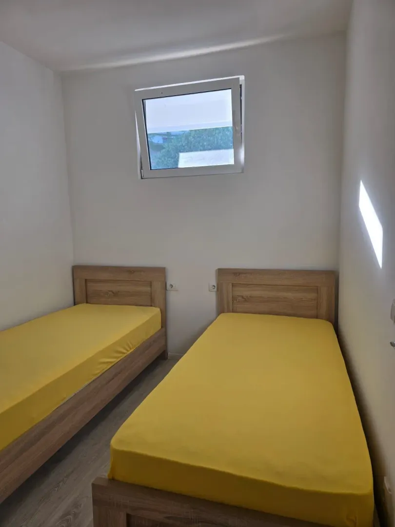 Manja spavaća soba sa dva drvena kreveta sa žutim posteljinama i prozorom na zidu.