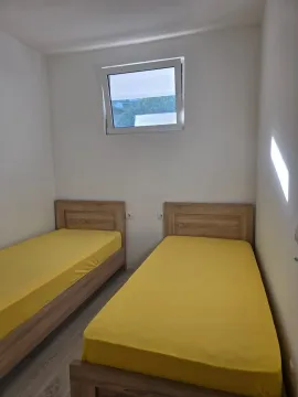 Manja spavaća soba sa dva drvena kreveta sa žutim posteljinama i prozorom na zidu. - image 7