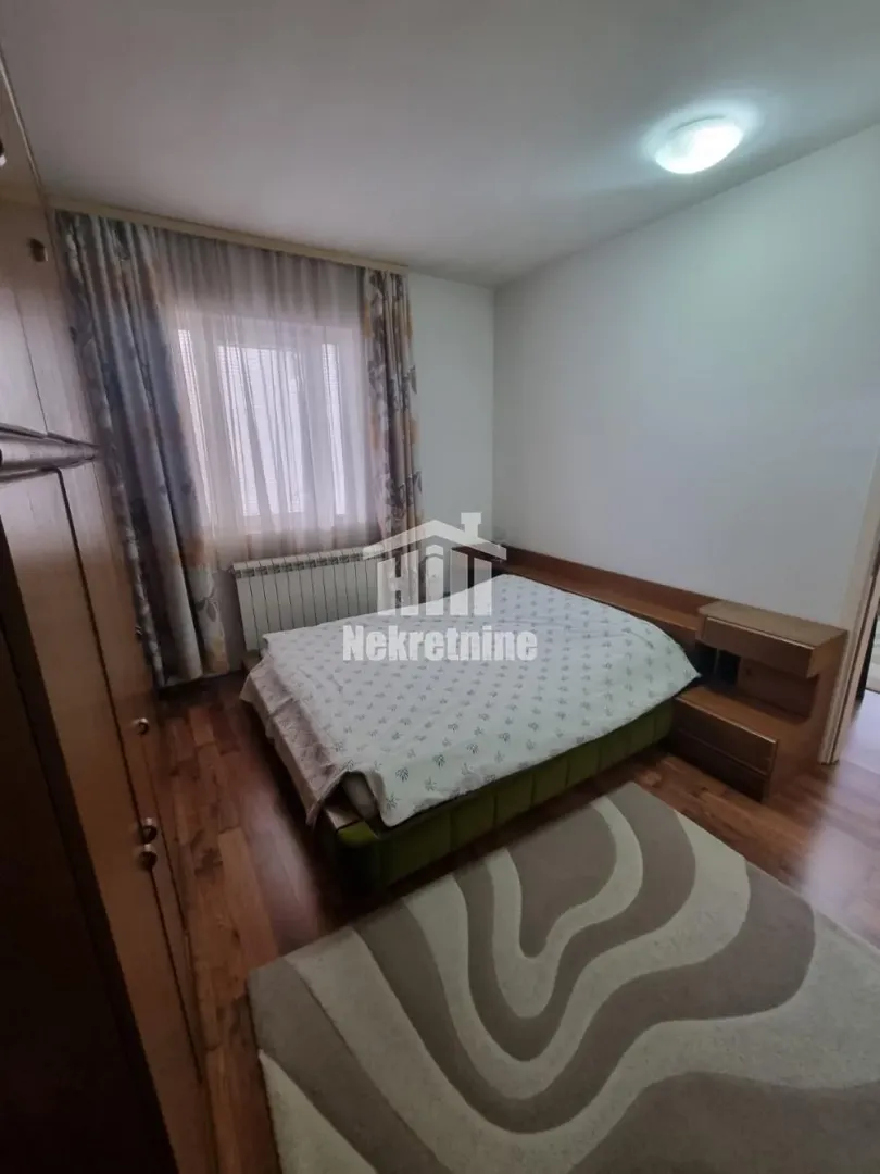 Nameštena spavaća soba sa bračnim krevetom, garderoberom i tepihom.