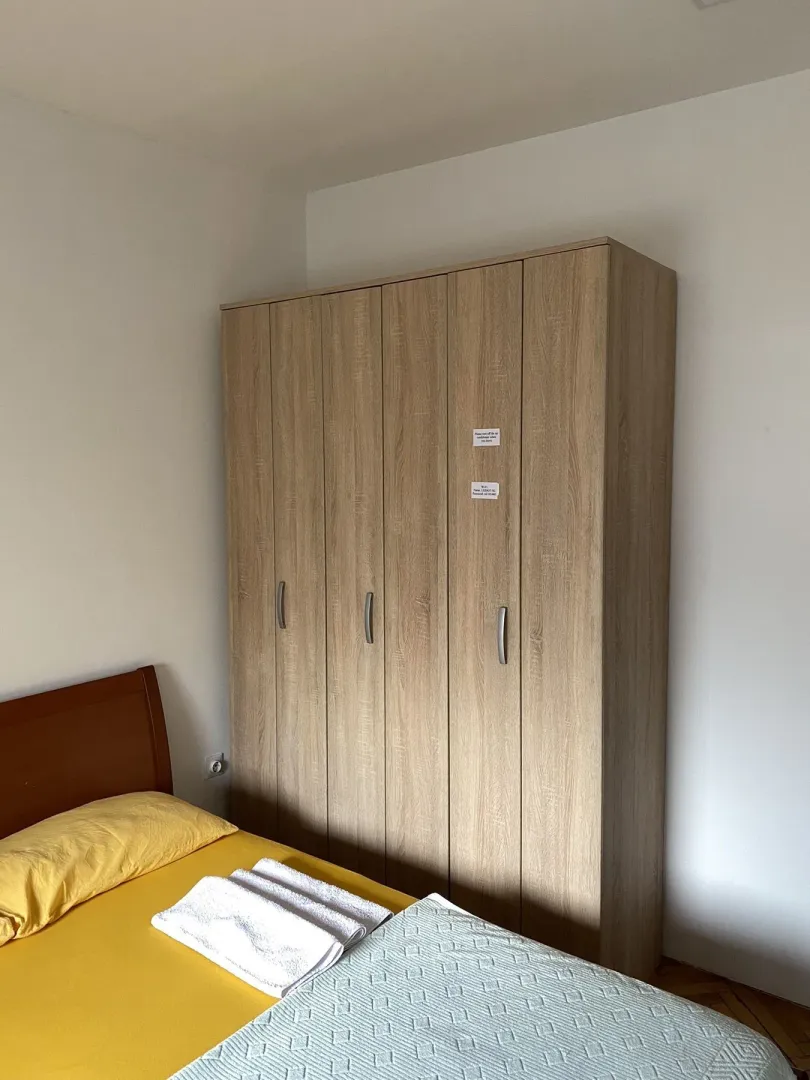 Jednostavna spavaća soba sa drvenim ormarom i krevetom.