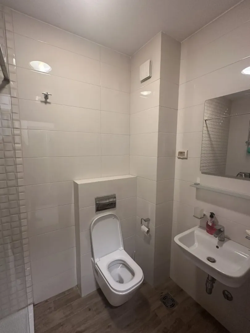 Svijetlo kupatilo sa bijelim pločicama, lavaboom i toaletnom šoljom.