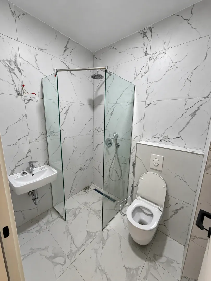 Moderne kupatilo obloženo keramičkim pločicama sa tuš kabinom i ugradnim wc šoljom.