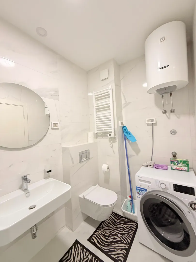 Svijetlo moderno kupatilo sa umivaonikom, WC šoljom, veš mašinom i bojlerom.