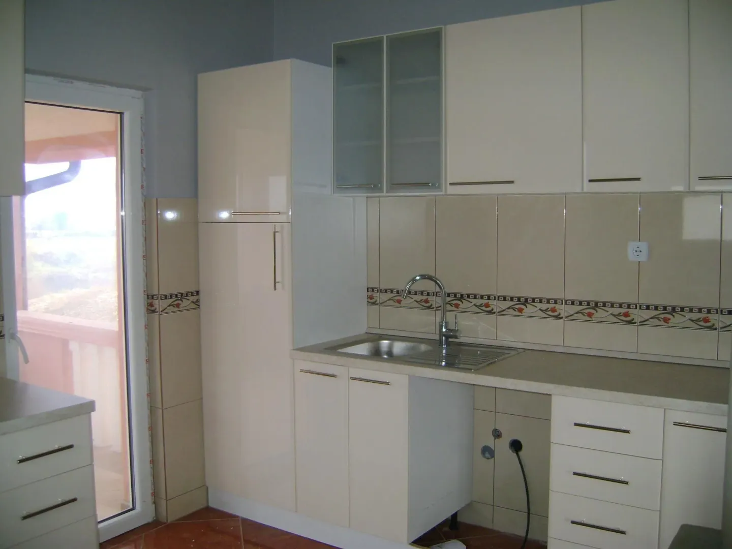 A kitchen with light beige cabinets, tiled backsplash, and a balcony door.