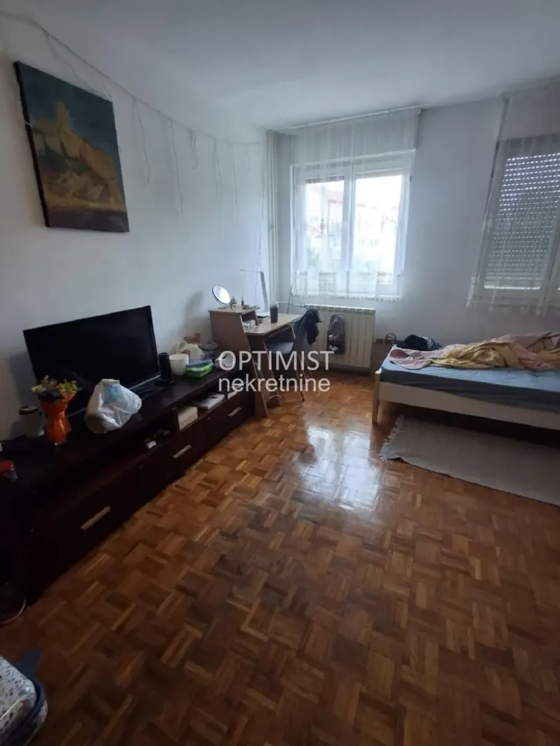 Nameštena spavaća soba sa krevetom, radnim stolom i televizorom.