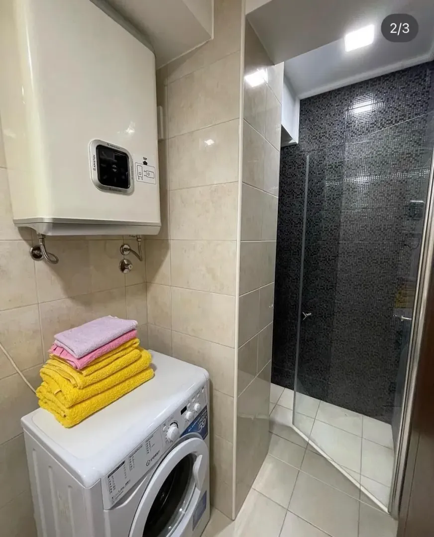 Smaller bathroom with a shower cabin, water heater, and washing machine.