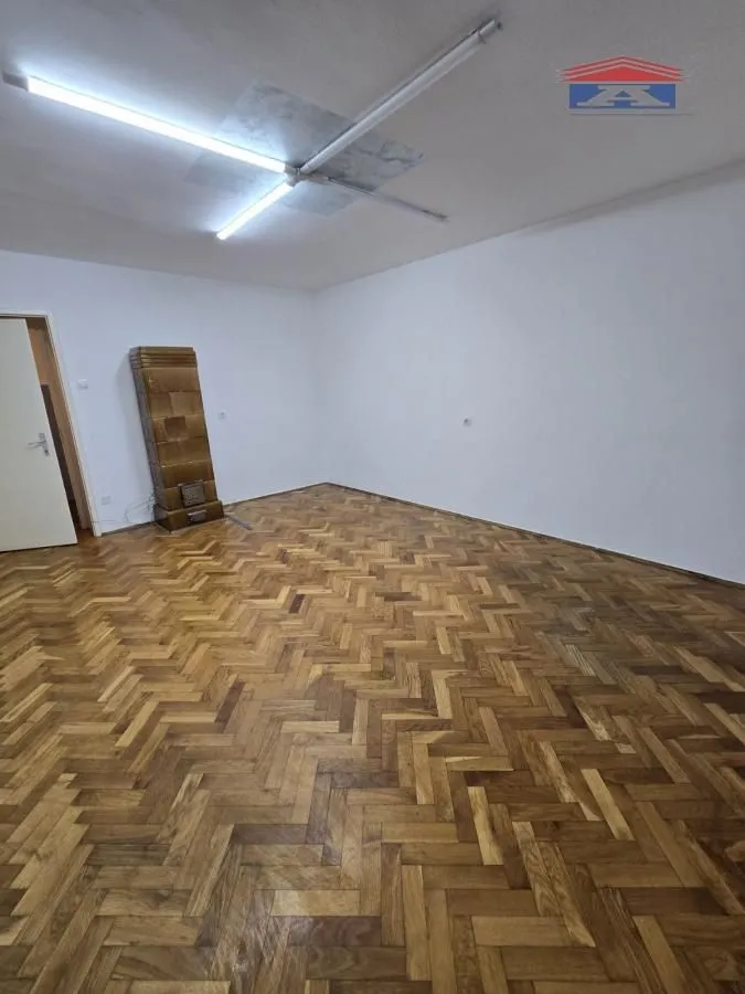 Empty room with wooden parquet flooring and a wood stove.