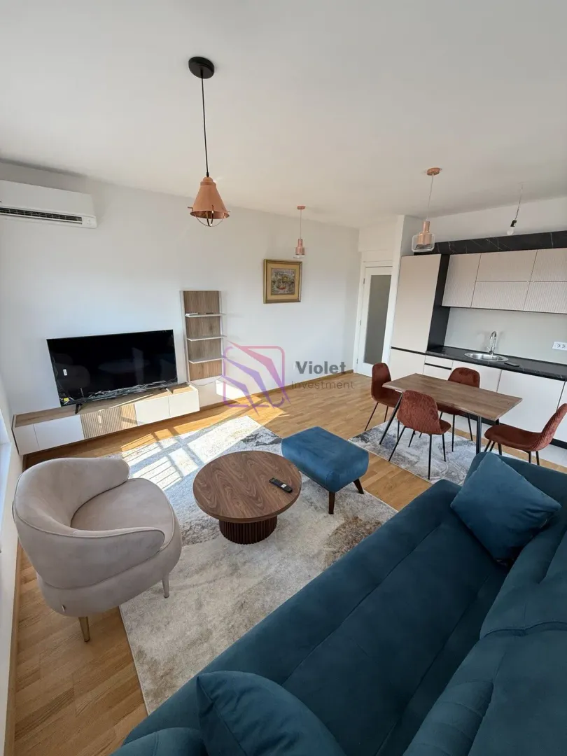 Living room with a sofa, TV, and a kitchen in the background.