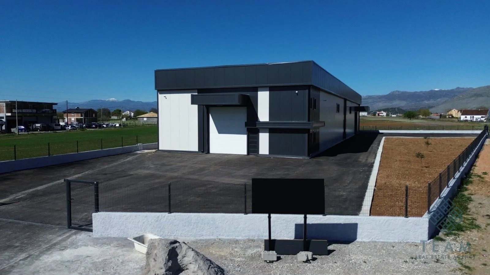 Aerial view of a modern commercial building with a warehouse and fenced courtyard.