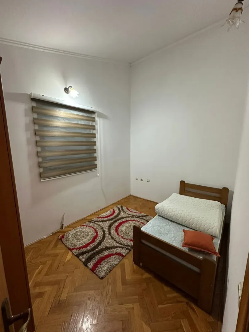 A small bedroom with a single bed, a patterned rug, and parquet flooring.