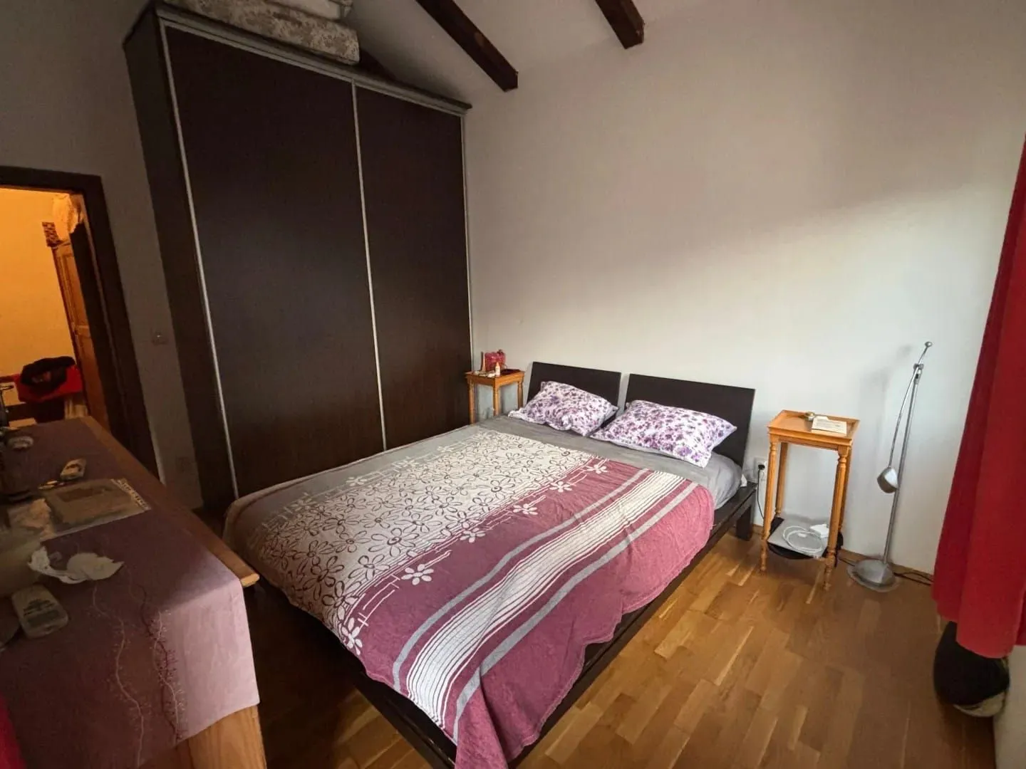 Namještena spavaća soba sa bračnim krevetom, plakarom i drvenim podom.