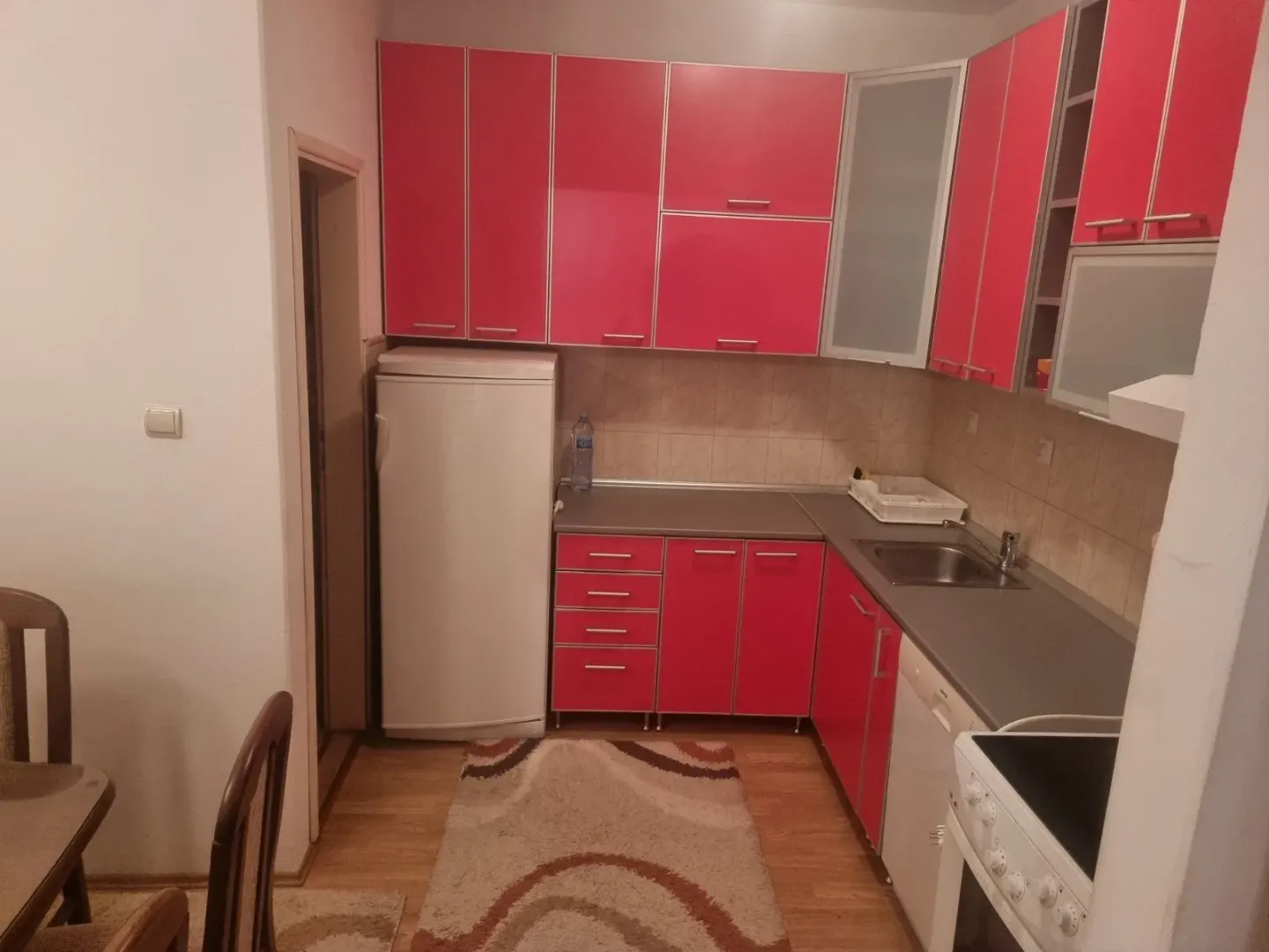Manja kuhinja sa jarko crvenim elementima i bijelom tehnikom.