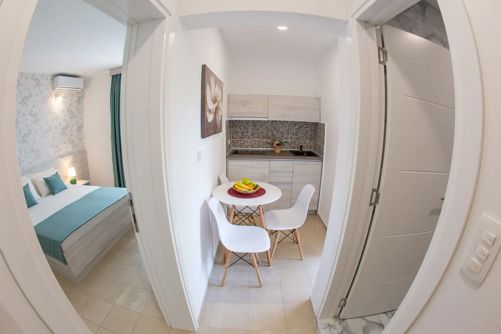 View from the hallway into the kitchen with a dining table and a bedroom.