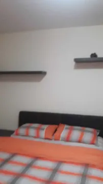 Spavaća soba sa narandžastom posteljinom i policama na zidu. - image 8
