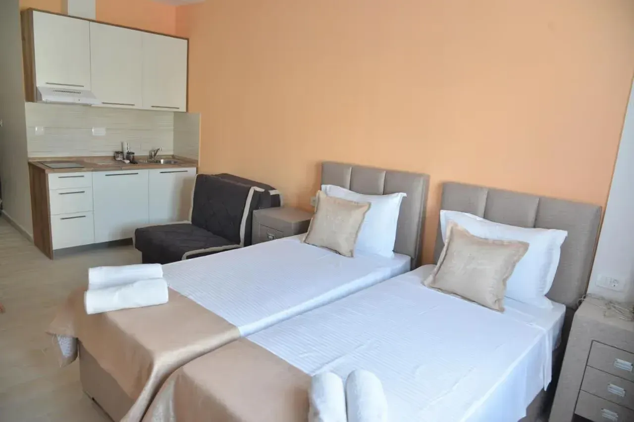 Bedroom with two single beds and a small kitchen in the background.