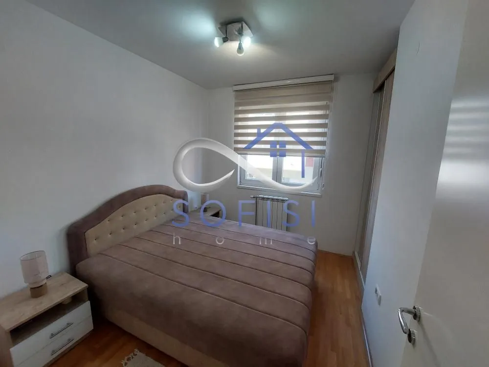 Nameštena spavaća soba sa bračnim krevetom, noćnim stočićem i prozorom.