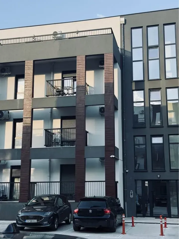 Spoljašnji izgled moderne stambene zgrade sa terasama i parkingom ispred.