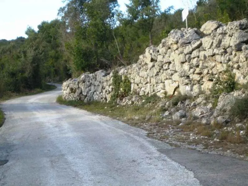 Asfaltirani prilazni put pored starog kamenog zida.