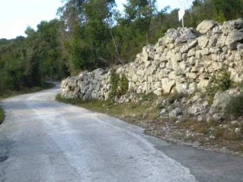 Asfaltirani prilazni put pored starog kamenog zida. - image 3