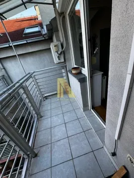Manji popločani balkon sa metalnom ogradom i pogledom na krovove zgrada. - image 9