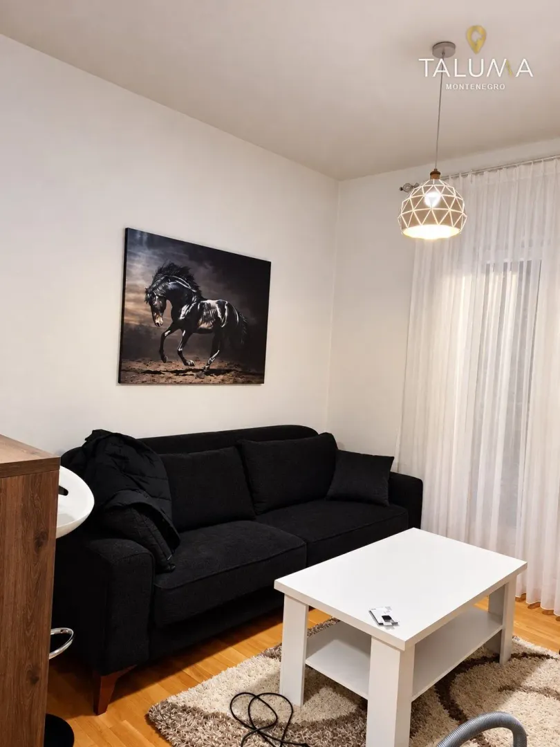 Living room with a black sofa, white coffee table, and an artwork on the wall.