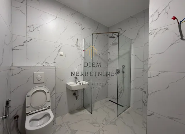 Moderne kupatilo obloženo mermernim pločicama sa tuš kabinom i wc šoljom.