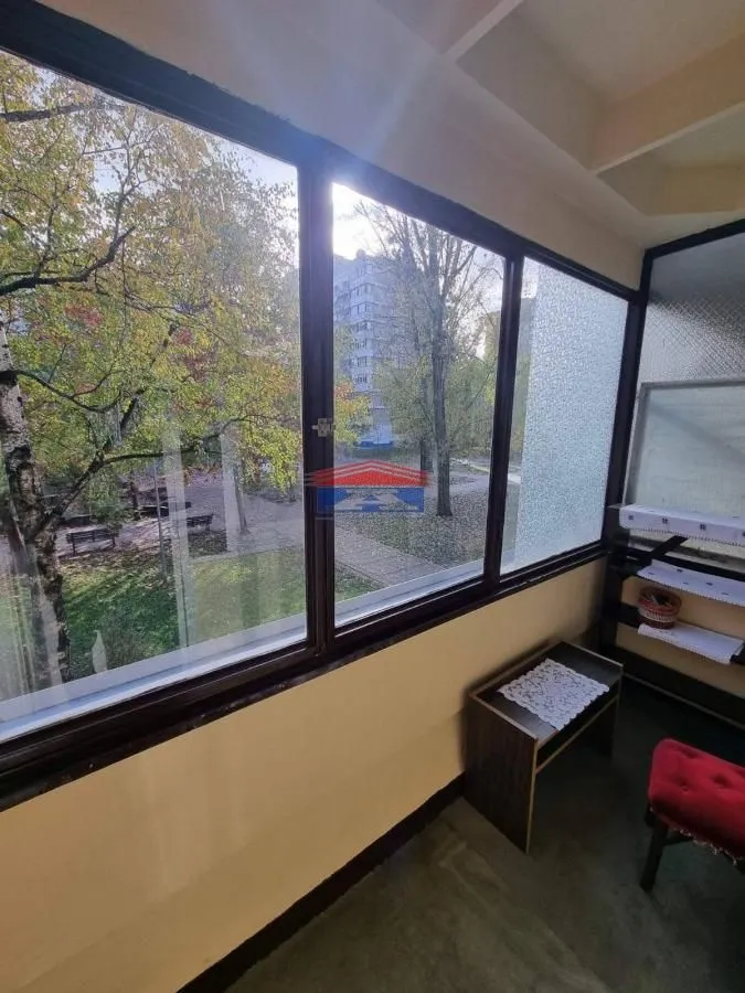 Zastakljeni balkon sa pogledom na dvorište i drveće.