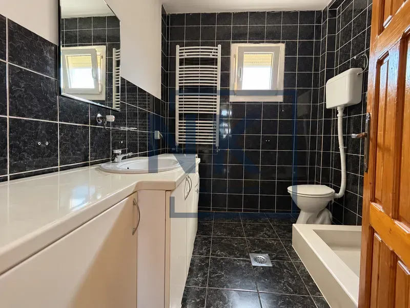 Kupatilo sa tamnim pločicama, umivaonikom i wc šoljom.