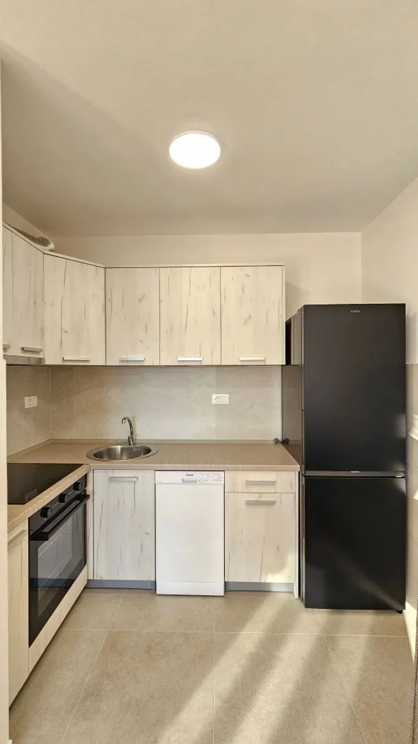 Compact bright kitchen with wooden cabinets and a black refrigerator.
