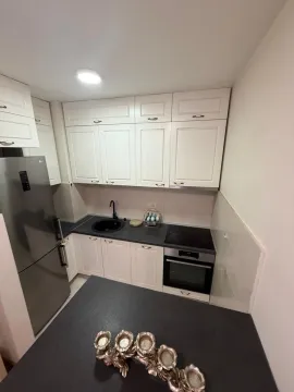 Kuhinja sa bijelim elementima, tamnom radnom površinom i ugradnim aparatima. - image 3