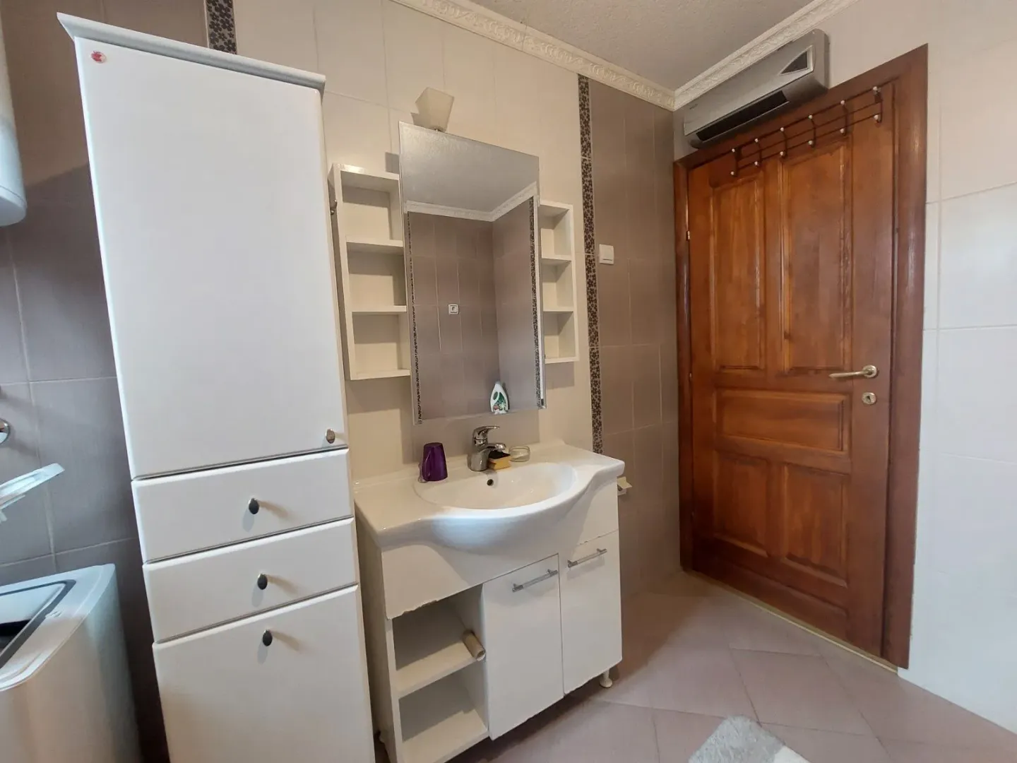 Manje kupatilo sa umivaonikom, ormarićem i drvenim vratima.