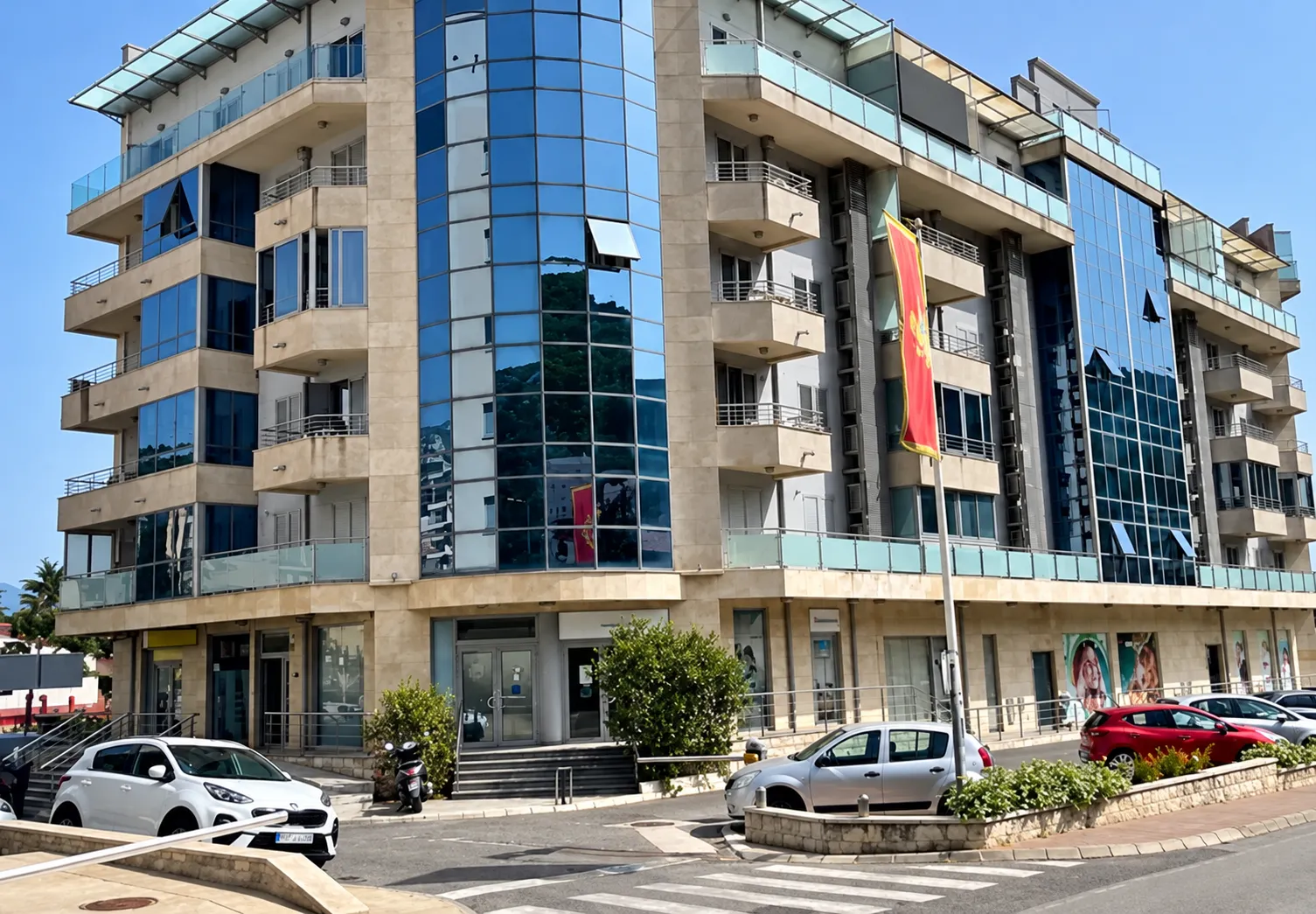 Exterior view of a modern multi-family building with glass elements and parked cars in front.