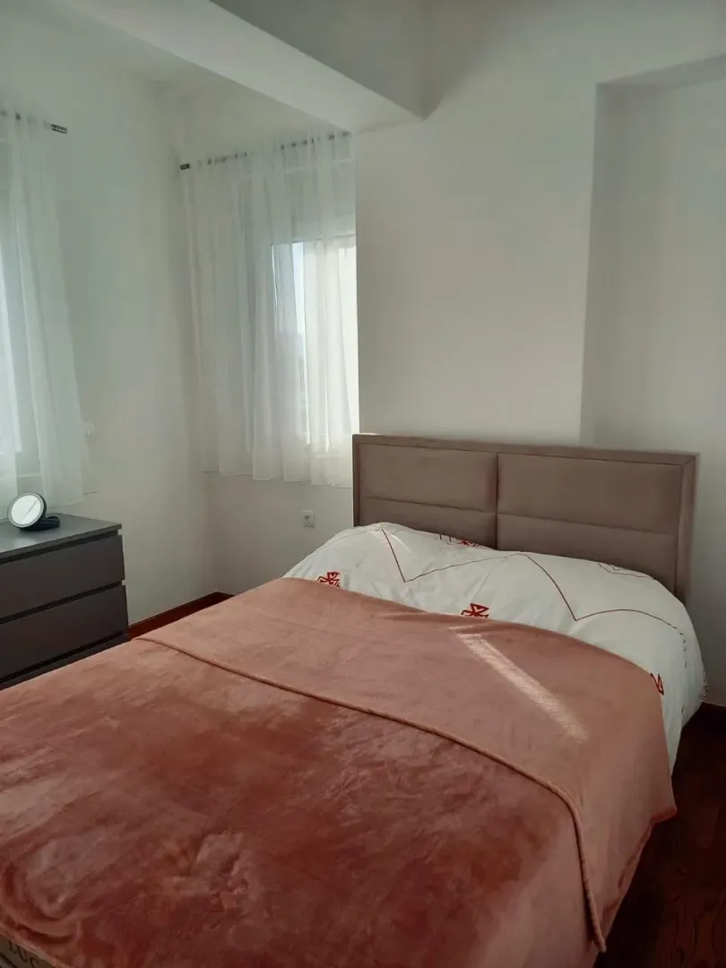 Bright bedroom with a double bed and a window with white curtains.