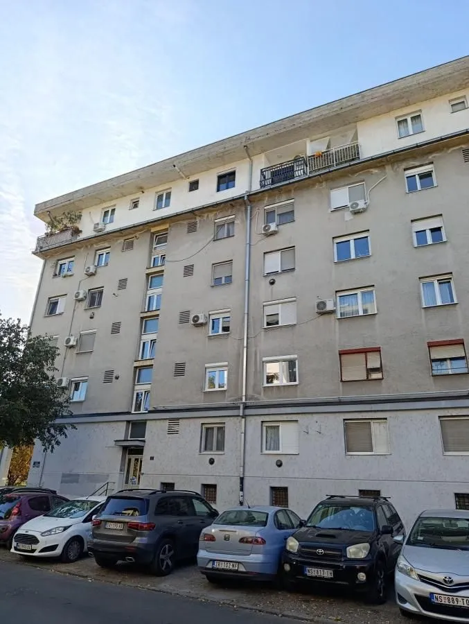 Fasada stambene zgrade sa parkingom i parkiranim automobilima.