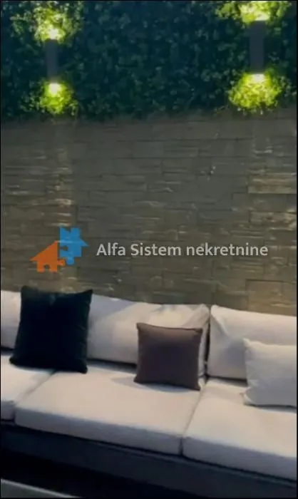 Uređena terasa sa garniturom za sedenje i dekorativnim osvetljenjem na zidu.