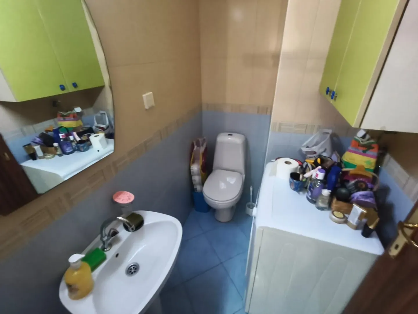Manje kupatilo sa umivaonikom, WC šoljom, mašinom za veš i zidnim elementima.