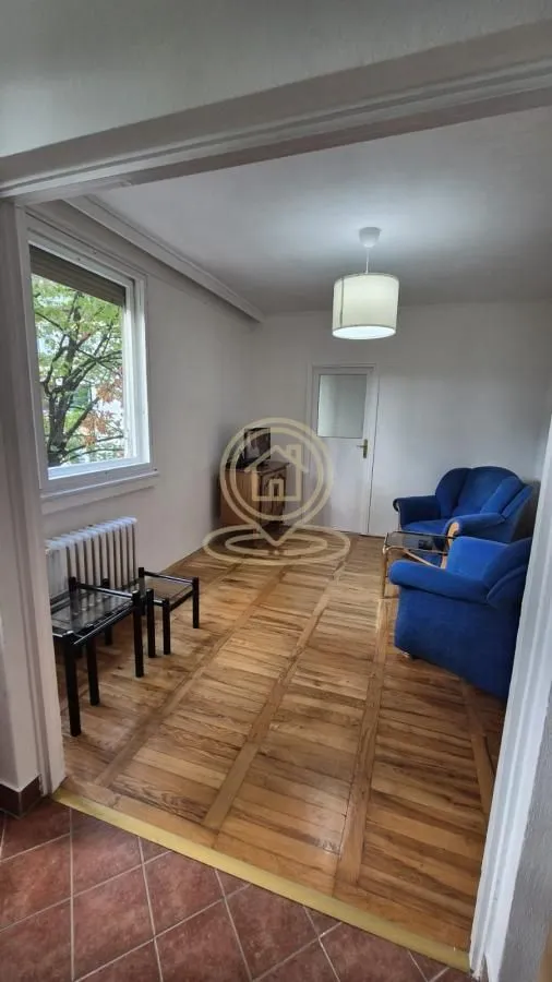 Dnevni boravak sa drvenim podom, plavim foteljama i prozorom.
