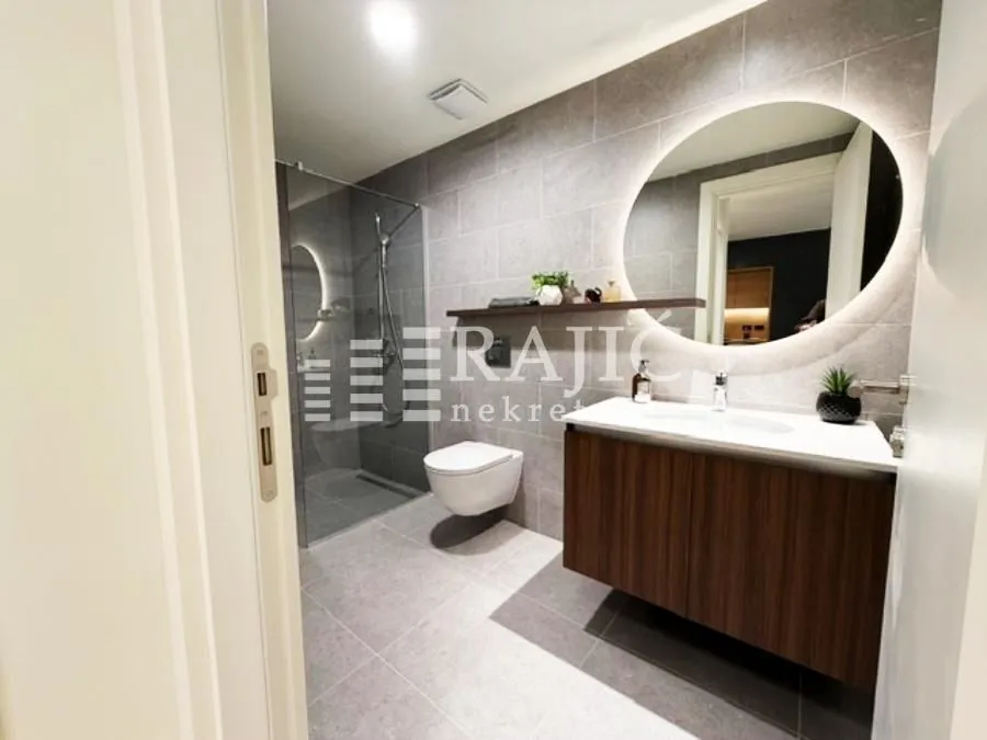 Modern bathroom with a walk-in shower, vanity sink, and illuminated mirror.