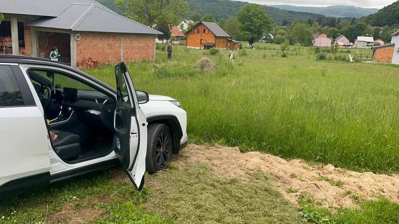 Pogled na dvorište sa kućom i parkiranim automobilom u prvom planu.