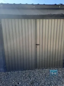 View of metal garage doors with gravel in the yard. - image 3