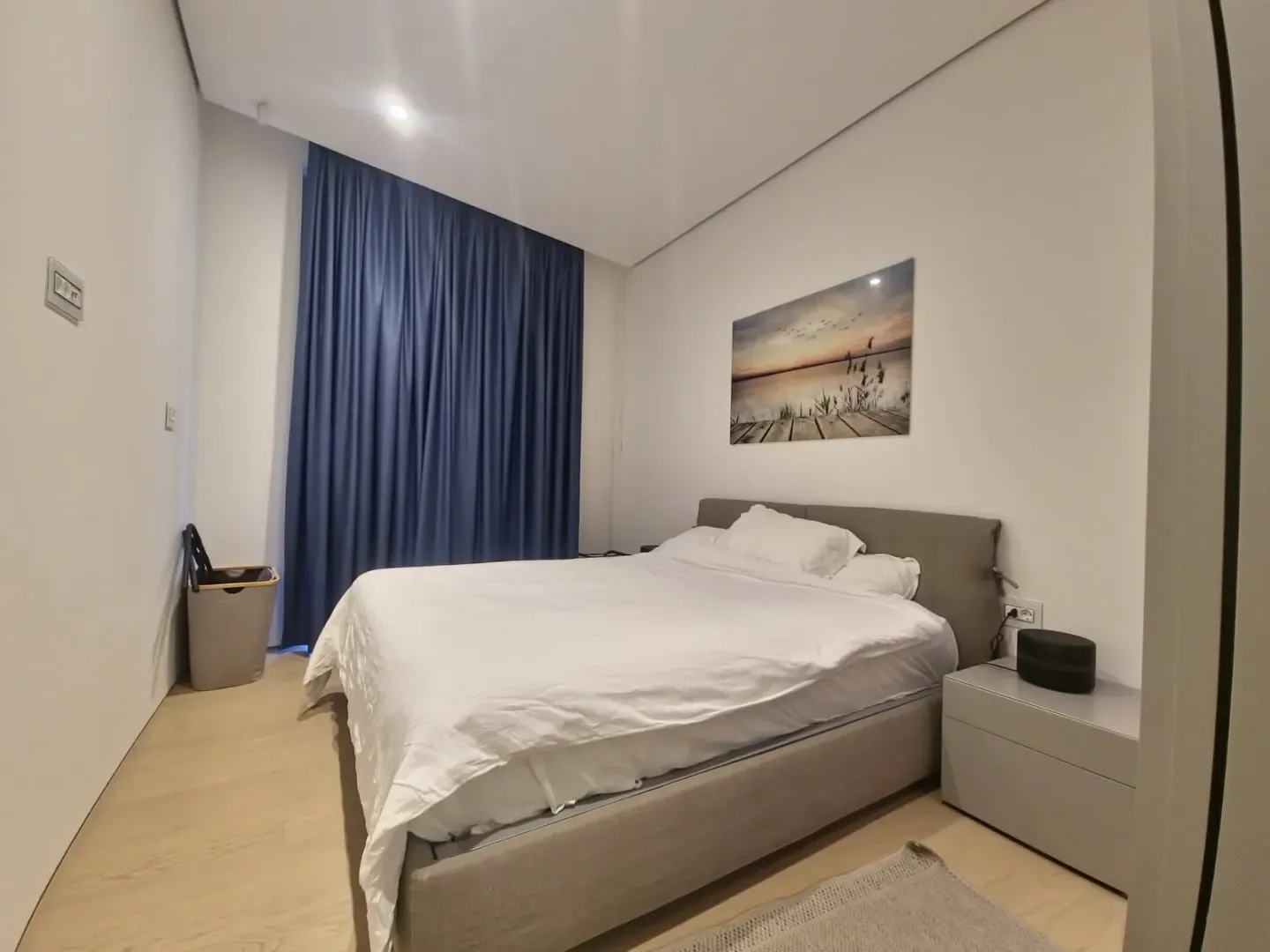 Modern bedroom with a double bed and a large window with blue curtains.