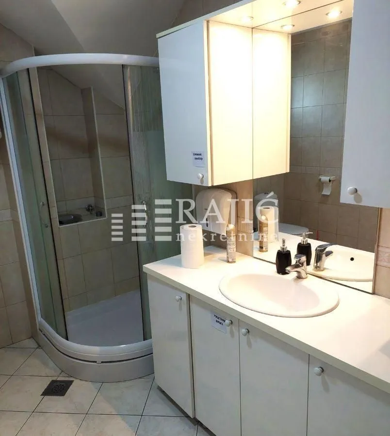 Compact bathroom with a shower cabin and a white washbasin.