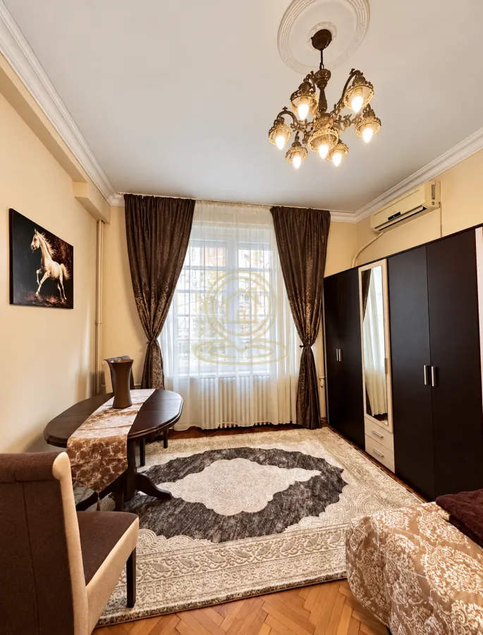 Nameštena spavaća soba sa bračnim krevetom, velikim garderoberom i trpezarijskim stolom.