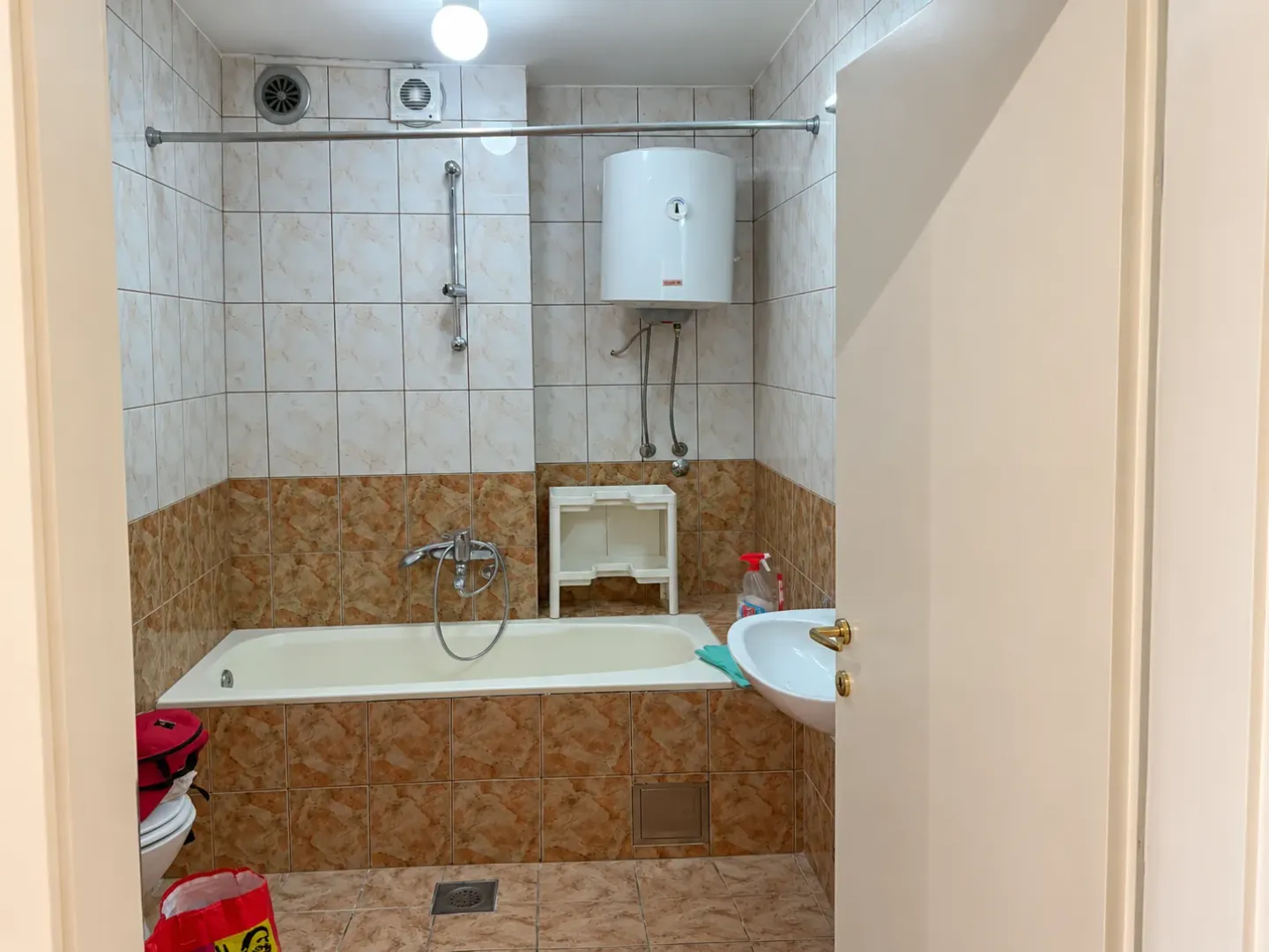 Bathroom with a bathtub, washbasin, and water heater tiled with ceramic tiles.