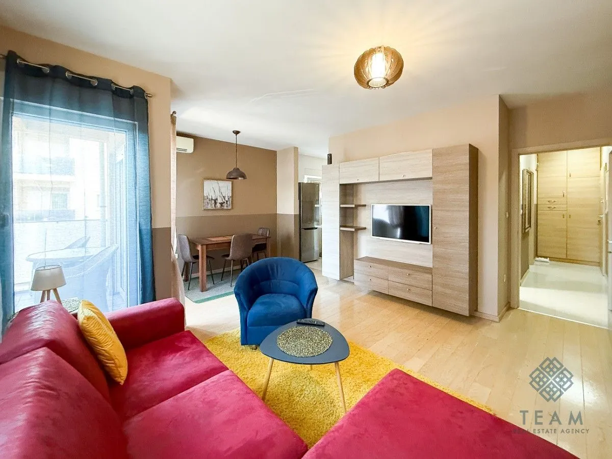 Living room with a sofa set, TV unit, and a dining area in the background.