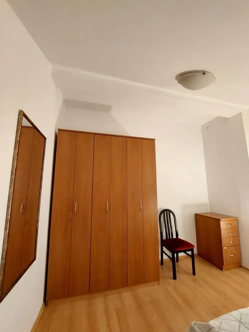 Small bedroom with a wooden wardrobe, chest of drawers, a chair, and a wall mirror.